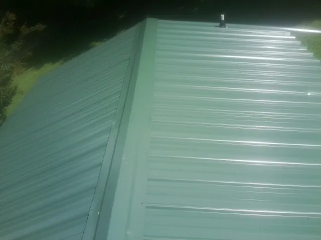 New green metal panels meeting at the ridge of a roof — Flat Roof Repair work by our crew in Delta