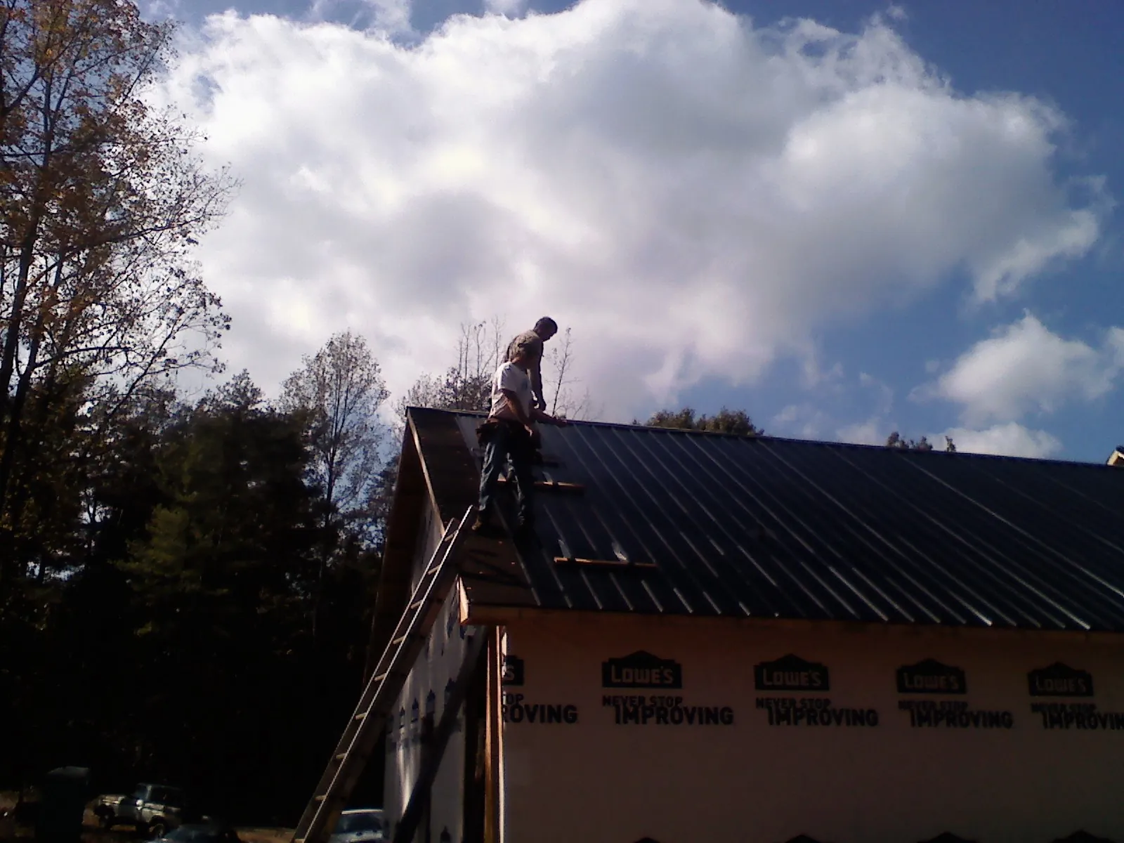 Roofer fastening dark metal panels high against a cloudy sky, from a Roof Inspection job in Delta