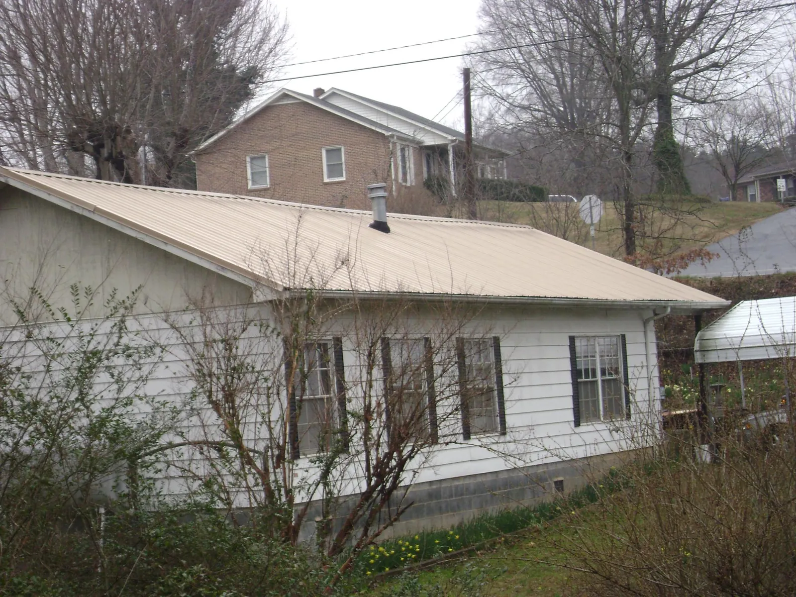 Tan metal roof on a white sided house set into a hillside — Commercial Roofing by Roofing Brothers in Delta